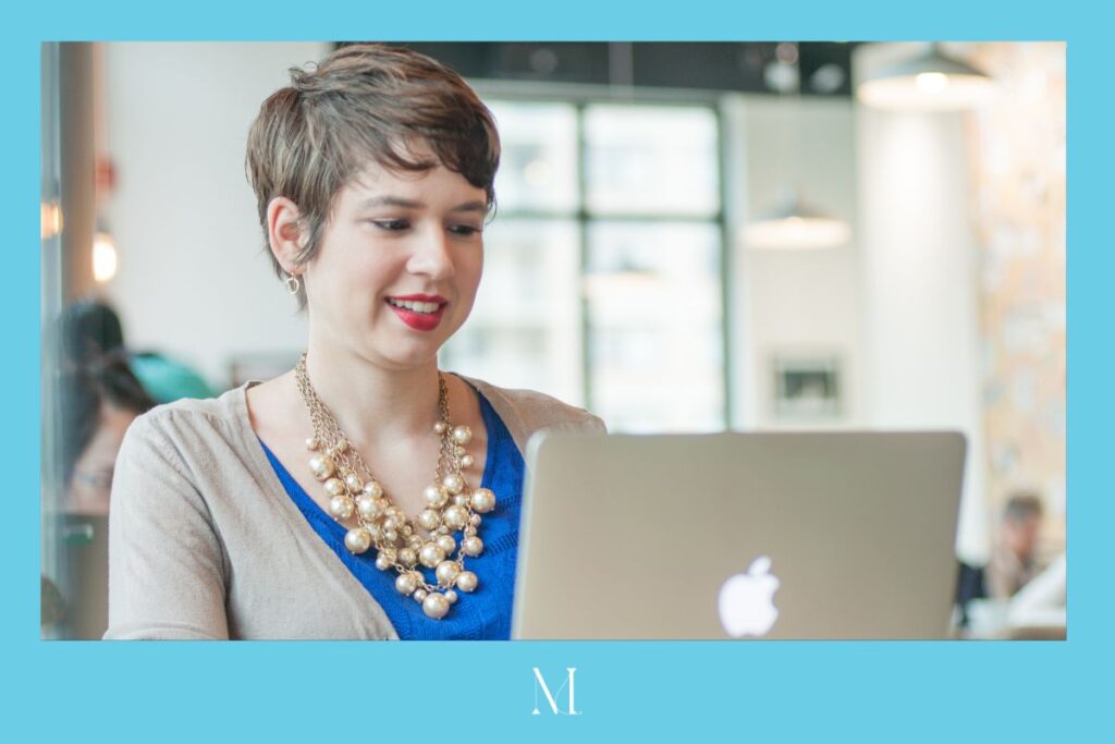 Eva has short brown hair and wears a blue shirt and pearl necklace. She is facing her silver laptop and smiling slightly